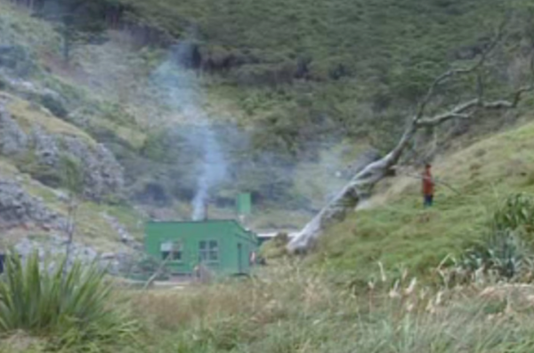 Man, who appears to be holding a rifle, near a hut at Whakapakari